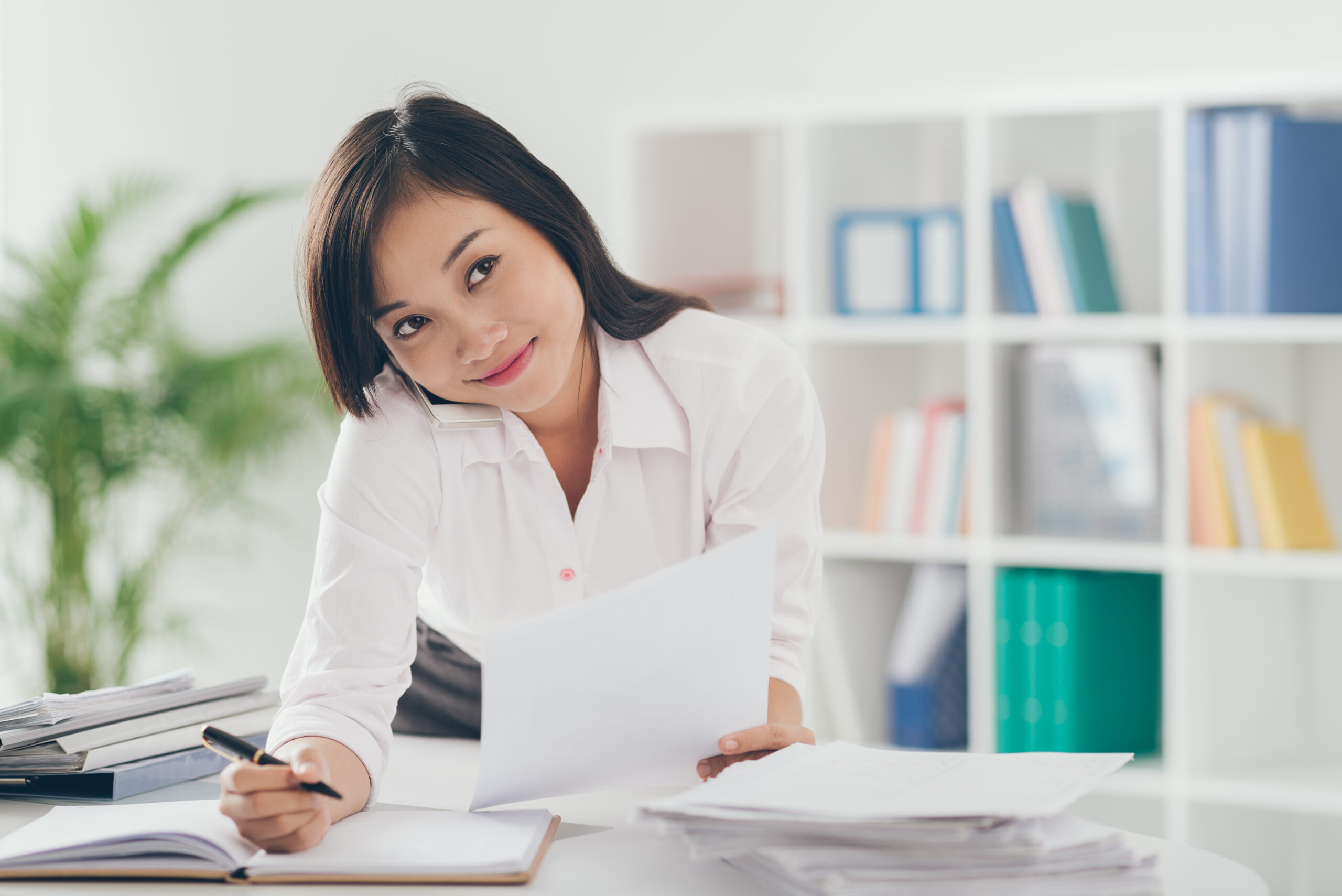 Pretty Asian manager talking on the phone and writing down in the office